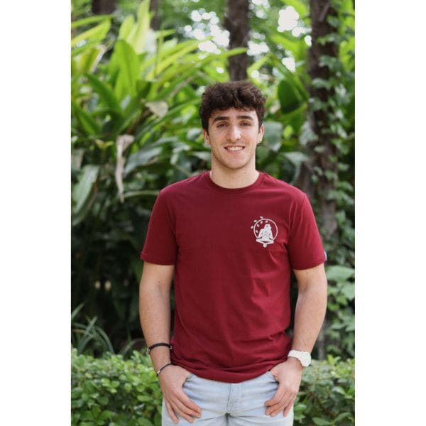 Hombre con Camiseta Burgundy Savannah de Flow Mico en burdeos con manos en bolsillos en entorno natural