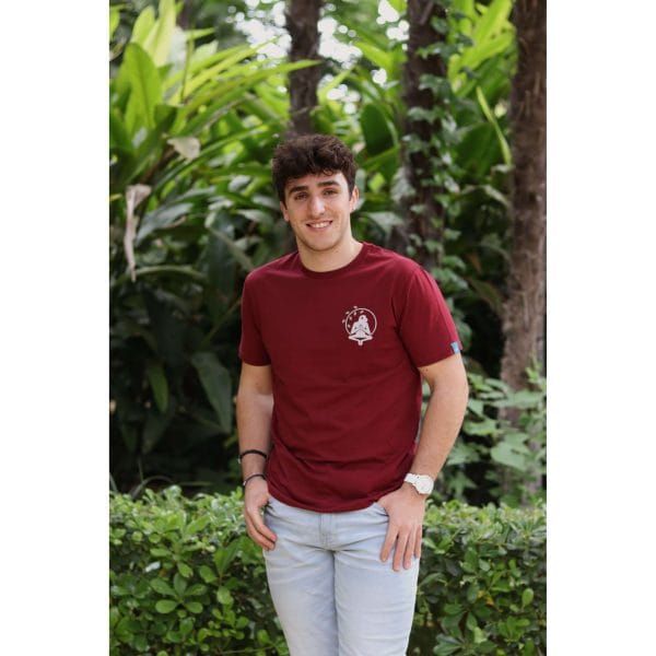 Hombre sonriendo con Camiseta Burgundy Savannah de Flow Mico en burdeos mostrando la etiqueta azul turquesa en manga