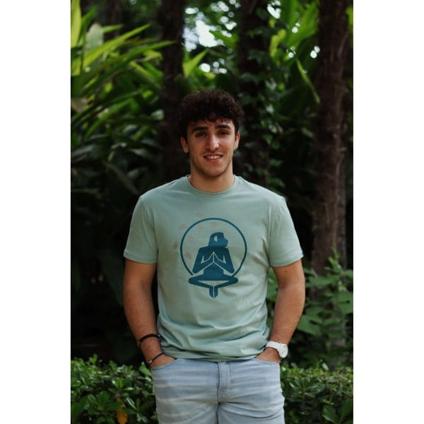 Hombre sonriendo con Camiseta Positano de Flow Mico en verde salvia con manos en bolsillos en entorno natural