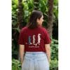 Vista trasera de mujer con Camiseta Burgundy Savannah mostrando la ilustración de tres suricatos y texto Flow Mico
