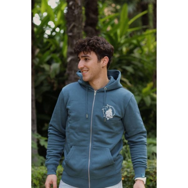 sudadera-balance-haven-hombre-lateral-2 Hombre sonriendo mirando a un lado con Sudadera Balance Haven de Flow Mico en azul petróleo en entorno natural