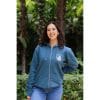 sudadera-balance-haven-mujer-frontal-3 Mujer sonriendo con Sudadera Balance Haven de Flow Mico en azul petróleo con cremallera y logo visible en entorno natural
