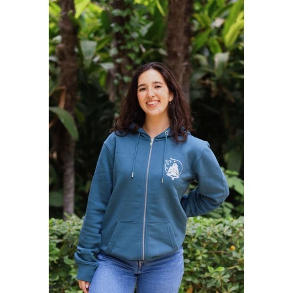 sudadera-balance-haven-mujer-frontal-3 Mujer sonriendo con Sudadera Balance Haven de Flow Mico en azul petróleo con cremallera y logo visible en entorno natural