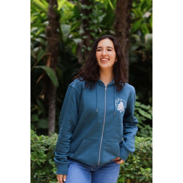 sudadera-balance-haven-mujer-frontal-2 Mujer sonriendo con Sudadera Balance Haven de Flow Mico en azul petróleo con cremallera y logo Flow Mico en el pecho