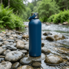 Botella térmica reutilizable azul de acero inoxidable junto a un arroyo en un entorno natural